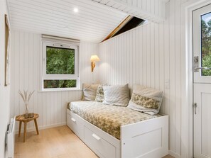 A bedroom with a bed, a window, a wall-mounted lamp, and a small table.