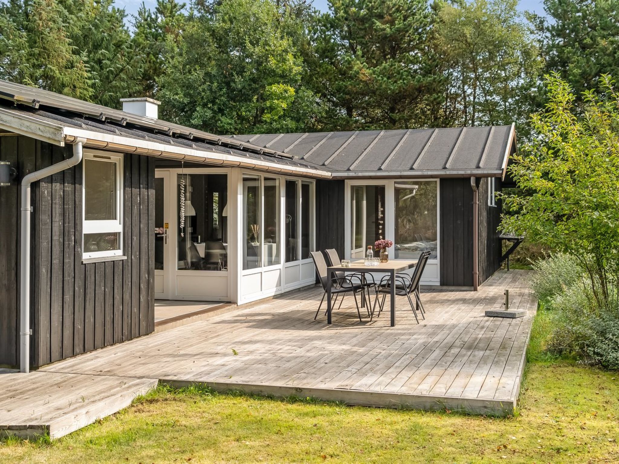 Une maison moderne dotée d’un patio couvert, d’un coin repas et d’une grande fenêtre donnant sur un jardin.