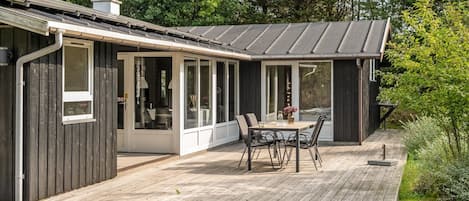 A modern house with a covered patio, a dining area, and a large window overlooking a garden.
