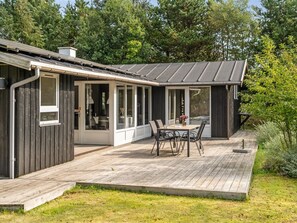 Een modern huis met een overdekte patio, een eethoek en een groot raam met uitzicht op een tuin.