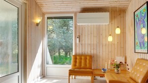 A cozy room with wooden walls, a large window, a sofa, a chair, and a small table with a vase. - "Orvokki" - 125m from the sea by Interhome (Sæby)