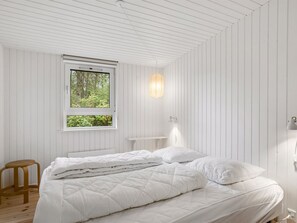 A bedroom with a bed, a window, a wall-mounted light, and a wooden stool.