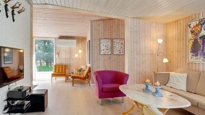 A modern living room with wooden panel walls, a sofa, a pink chair, a marble coffee table, and a television on the left. - "Orvokki" - 125m from the sea by Interhome (Sæby)