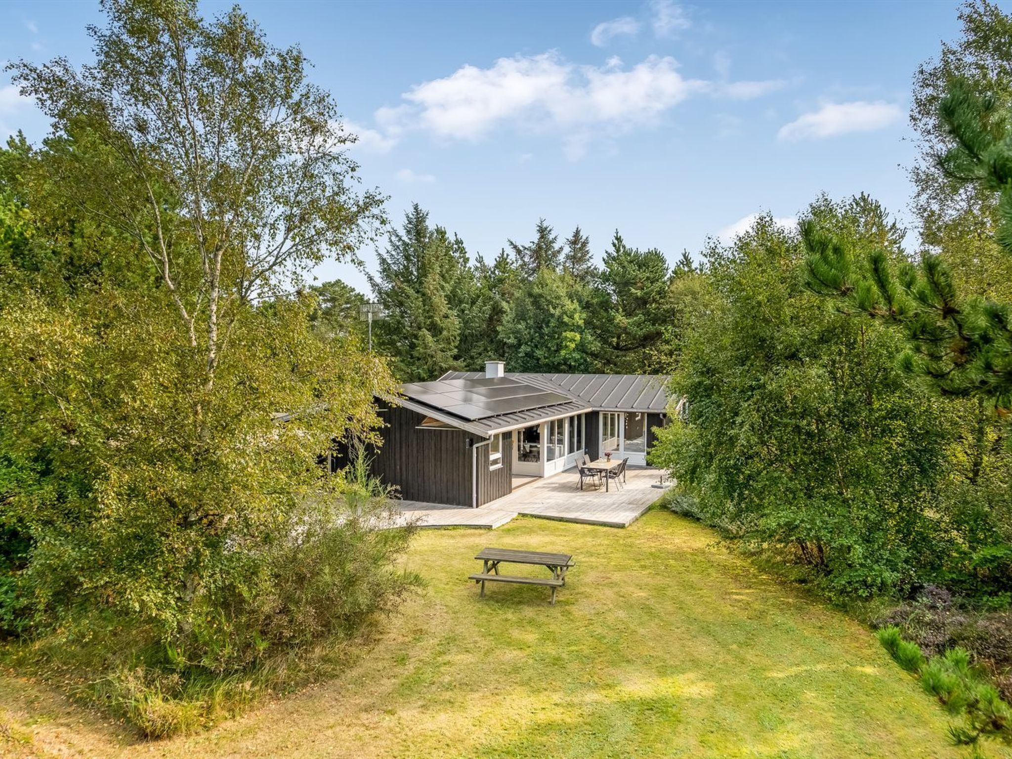 Ett modernt hus med en stor terrass, omgivet av täta träd.