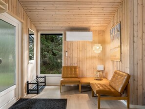 Une pièce aux murs en bois, avec un banc, une table et une fenêtre donnant sur un paysage verdoyant.