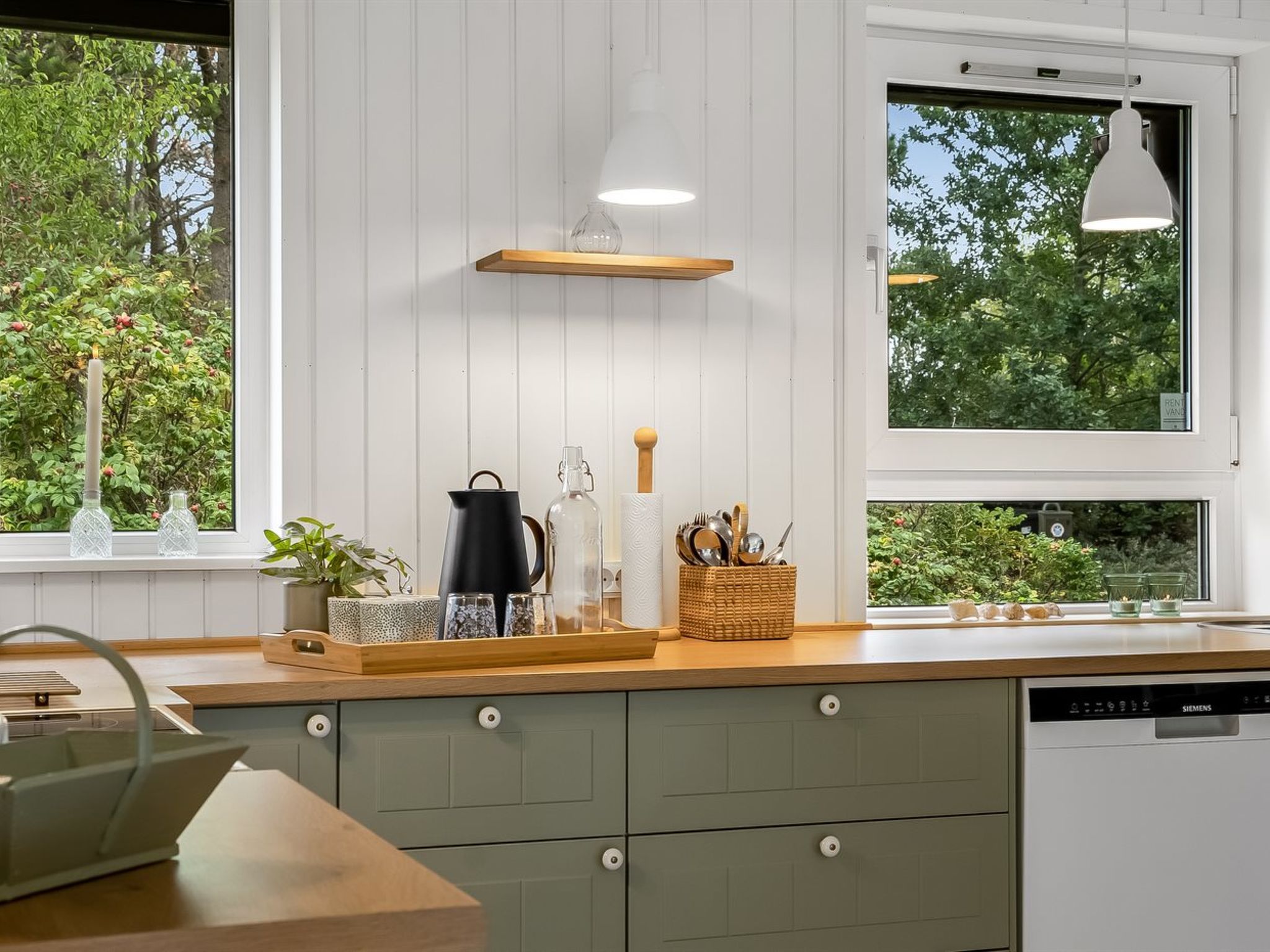 Een moderne keuken met een vaatwasser, een houten aanrechtblad en een raam met uitzicht op groen.
