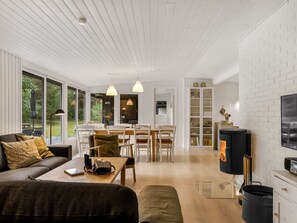 A modern living room with a sofa, dining table, and chairs, a fireplace, and large windows.