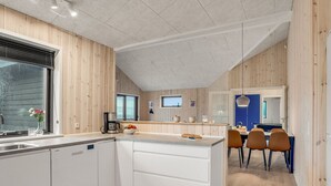 Una cocina moderna con paneles de madera, una isla central, muebles blancos y un comedor con sillas y una mesa.