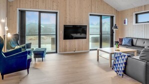 Amplia sala de estar con paredes de madera, un televisor grande y vistas al exterior.