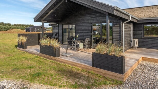 Una casa moderna con porche cubierto, ventanas amplias y mobiliario exterior.