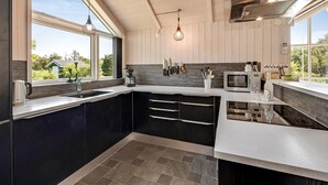 Une cuisine moderne dotée d’une grande fenêtre, de meubles de rangement aux couleurs sombres et d’un plan de travail blanc.