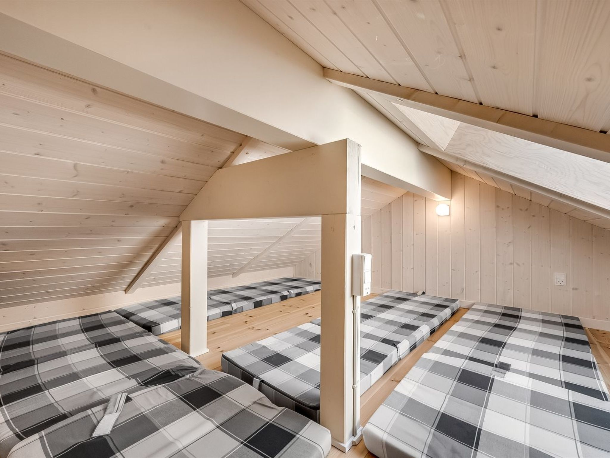 Ein Schlafraum im Schlafsaalstil mit Etagenbetten und Hochbett, Holzwänden und einer geneigten Decke.