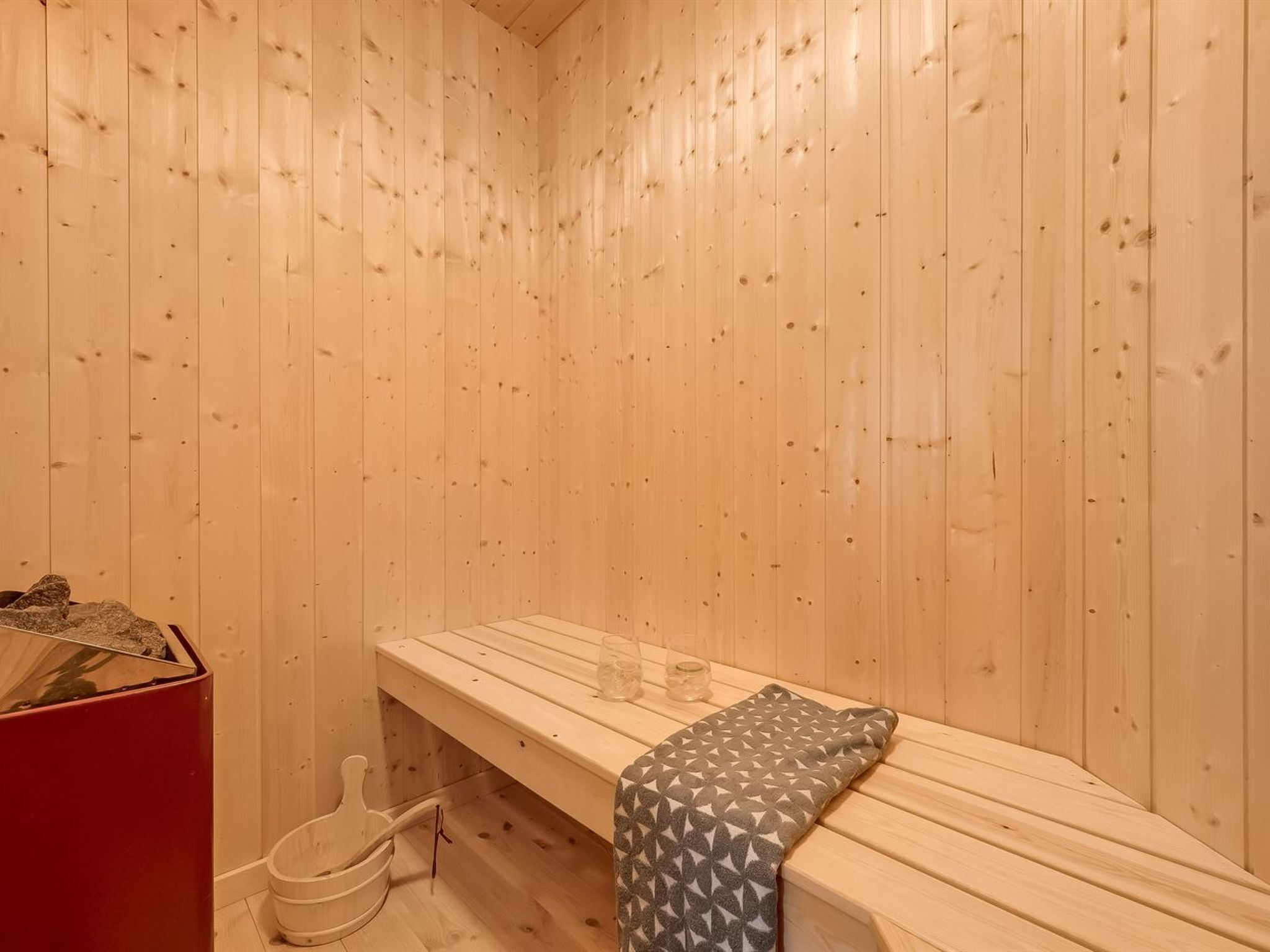 A sauna room with wooden walls, a bench, and a red cabinet.