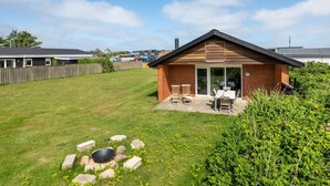 Een klein huis van baksteen met een terras, een vuurkorf en een omheinde tuin.