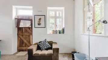 A cozy room with a brown sofa, a wooden door, a window with books, and a lamp.