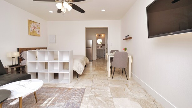 Un dormitorio moderno con cama, escritorio, silla, televisor y ventilador de techo.
