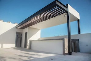 A modern building with a flat roof, a covered outdoor area with a metal roof, and a garage.