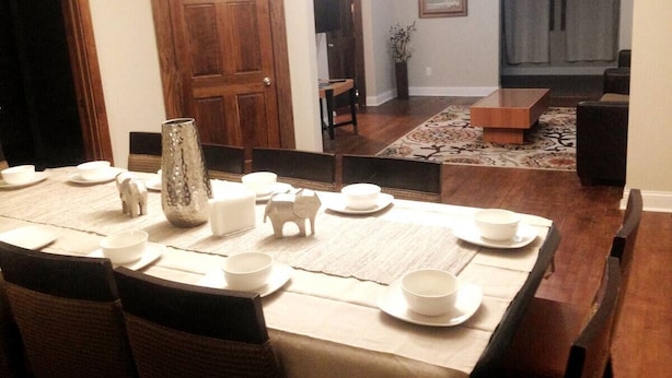 Un coin repas avec une longue table dressée pour quatre personnes, des chaises, un vase et une petite figurine d’éléphant.