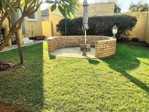 Eine runde Terrasse aus Ziegelsteinen mit einem kleinen Springbrunnen, umgeben von einem gepflegten Rasen.