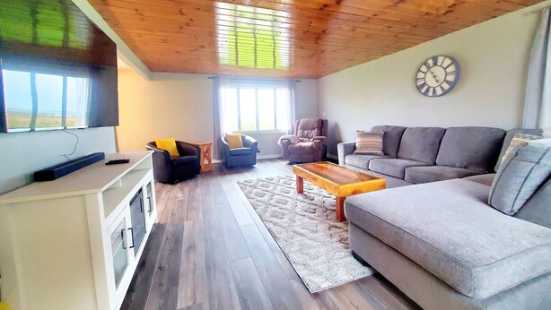 Un salón espacioso con techo de madera, un sofá gris, un sillón negro y una mesa de centro de madera.