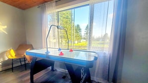 Una mesa de billar en una habitación con un ventanal grande, techo de madera y una silla.