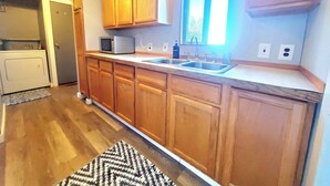 Cocina con armarios de madera, microondas, fregadero y ventana.