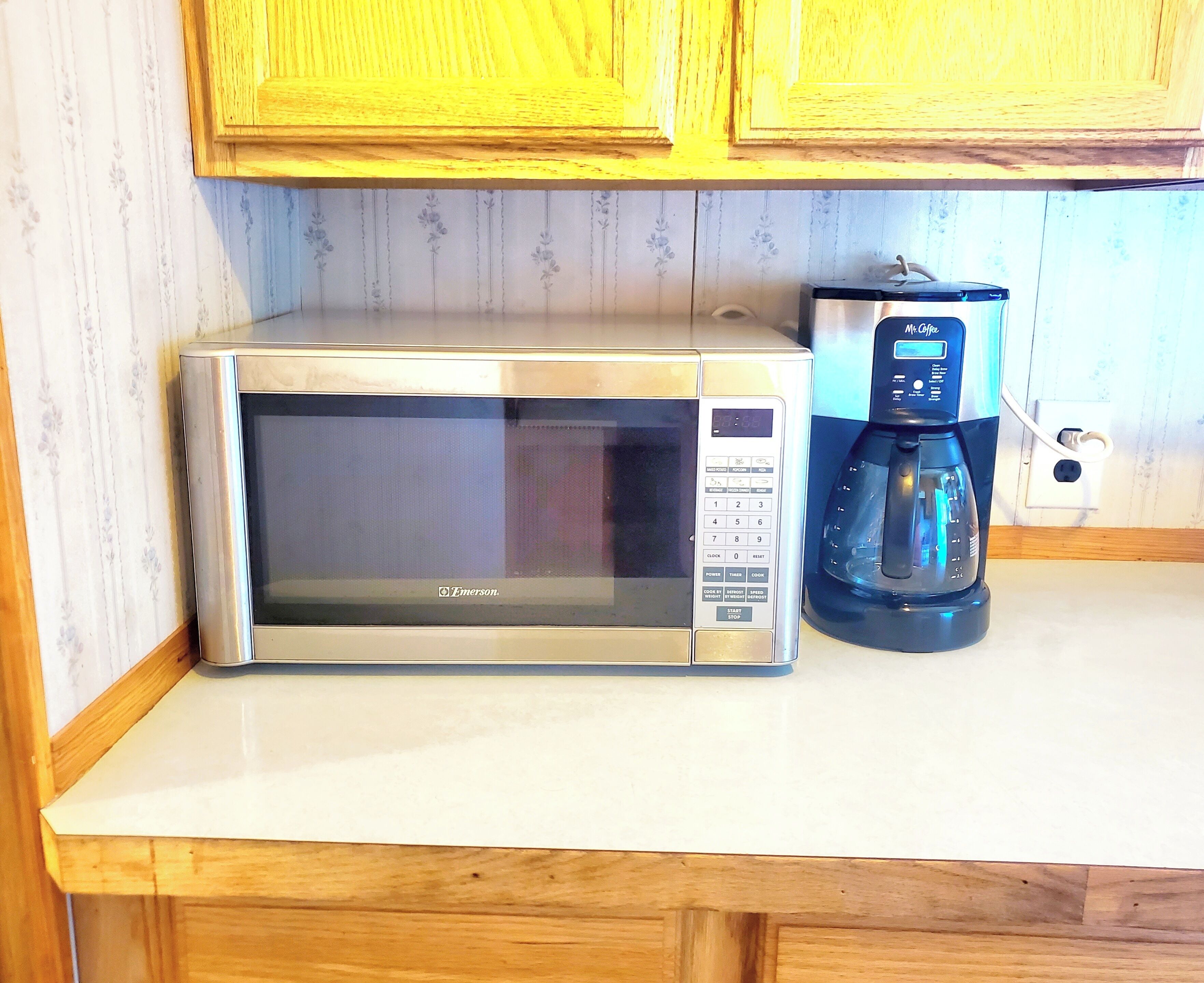 Un microondas y una cafetera sobre una encimera de cocina con armarios de madera arriba.
