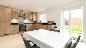 A modern kitchen with wooden cabinets, a large island, and a view of a brick wall and greenery outside. - 5 Bed House - Sleeps 9 - Pets - Garden - Parking (Ashford)
