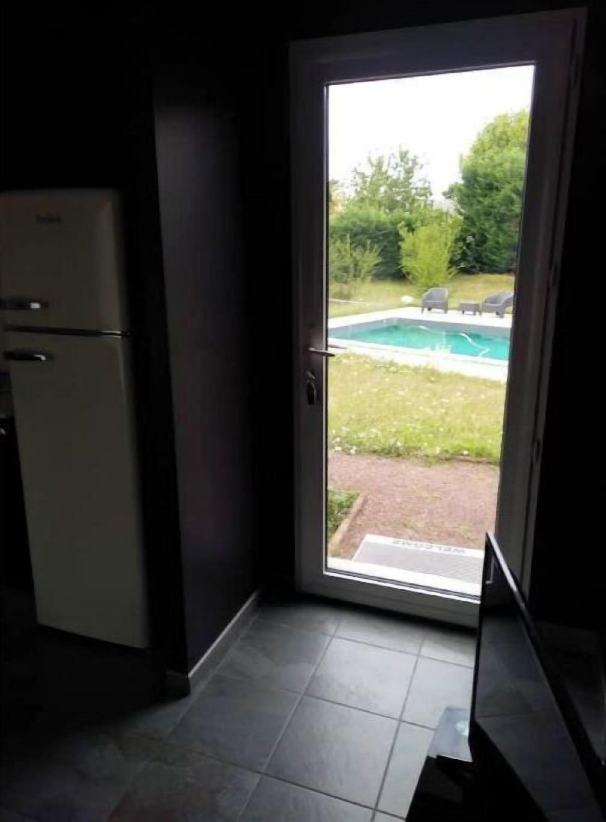 Une cuisine équipée d’un réfrigérateur et d’une porte donnant sur un jardin avec une piscine et un espace salon extérieur.