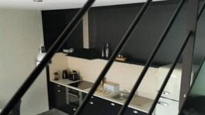 Una cucina compatta con mobili neri, un piano di lavoro e un lavello. Sono presenti due sedie nere e un tavolino.