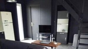 Un soggiorno moderno con zona pranzo, una sedia nera e un tavolino. C'è una televisione montata a parete e una scala che conduce a un altro piano.