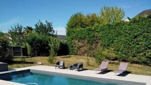 Una piscina rettangolare con bordo in cemento, circondata da erba e alberi.