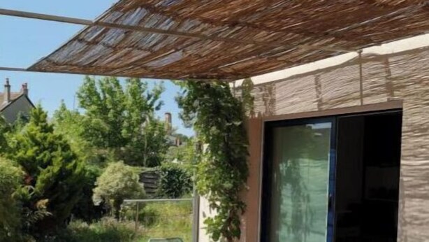 Una terrazza esterna con tavolo e sedie, un pergolato e vista su una zona residenziale.