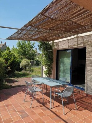 An outdoor patio with a table and chairs, a pergola, and a view of a residential area. - Petite de Maison (La Flèche)