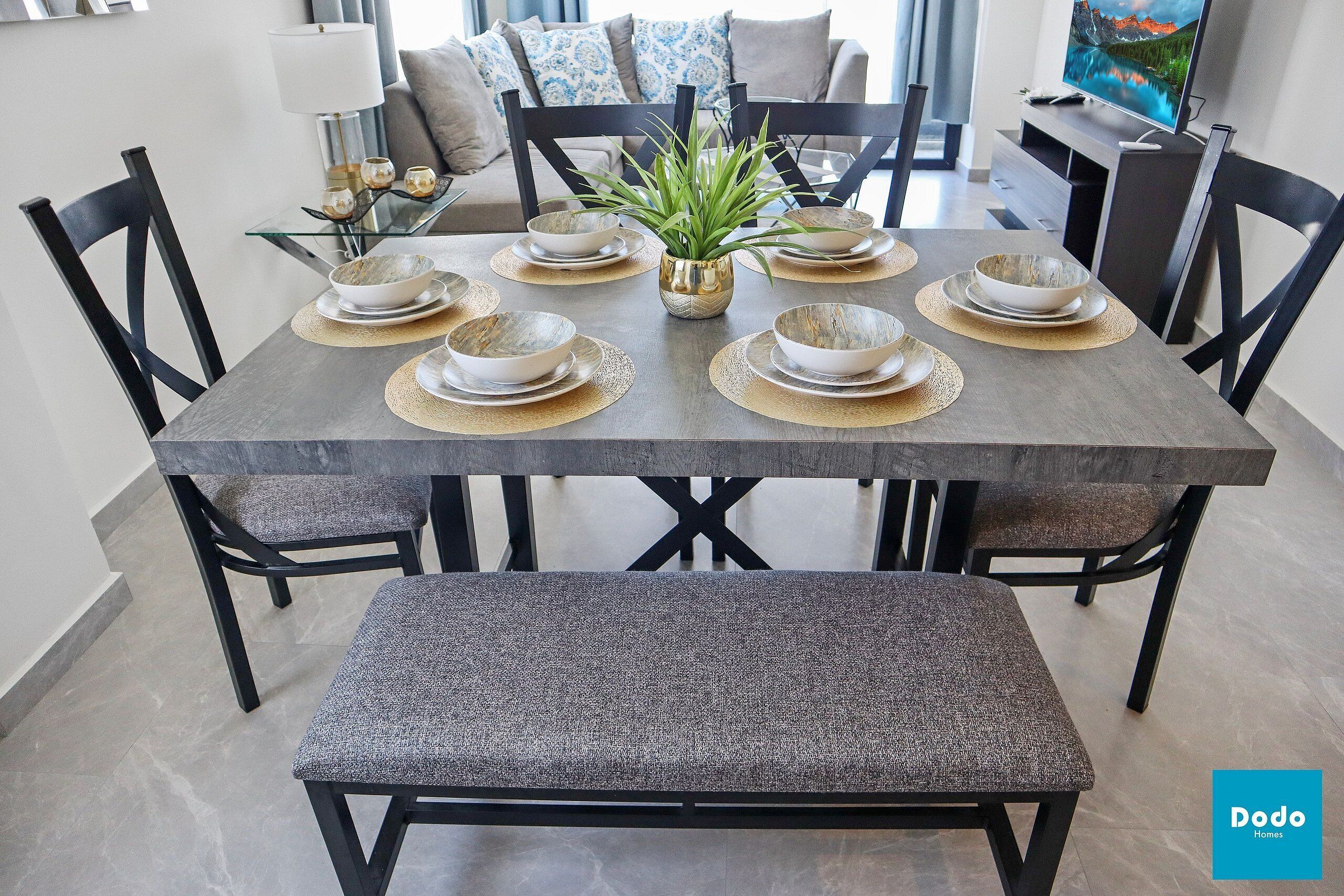 A dining area with a rectangular table set for four, surrounded by black chairs. A bench is placed in front of the table.