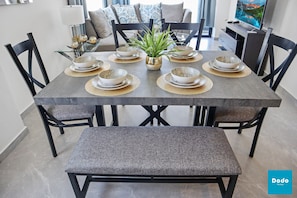 A dining area with a rectangular table set for four, surrounded by black chairs. A bench is placed in front of the table.