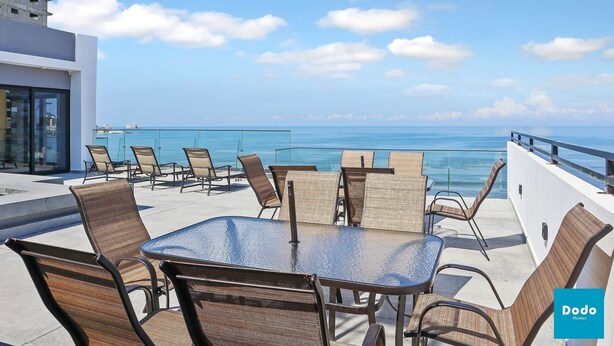 Eine Dachterrasse mit Glastisch und Stühlen, mit Blick auf einen klaren, blauen Himmel und den Ozean.