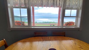 A wooden dining table with a cup, two chairs, and a window with a view of a body of water and greenery. - Spaniard's Perch - Incredible Ocean View (Spaniard's Bay)