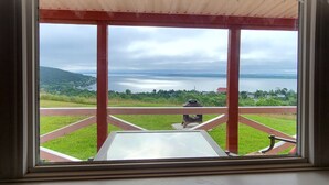 A view from a room with a large window overlooking a grassy area and a body of water. - Spaniard's Perch - Incredible Ocean View (Spaniard's Bay)