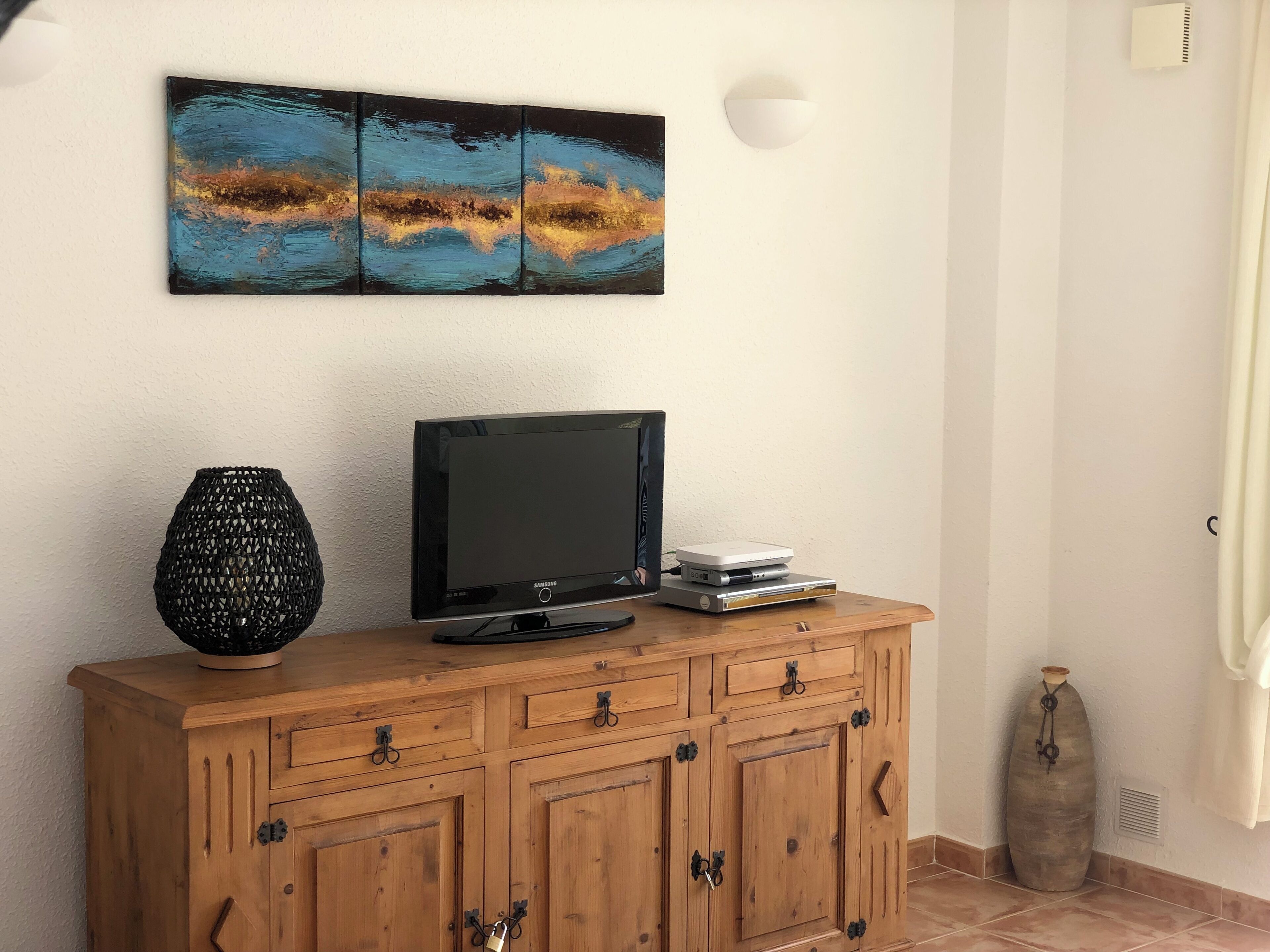 A wooden cabinet with a flat-screen TV, a decorative vase, and a wall-mounted abstract painting.