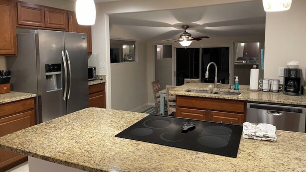 A modern kitchen with granite countertops, stainless steel appliances, and pendant lighting. - Coco NoKo cozy beach cottage + Swimming pool! Golf cart and pet friendly! (Nokomis)