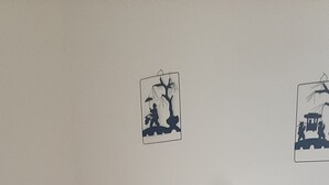 Un lit recouvert d’une couette grise, un mur blanc et deux tableaux accrochés au mur représentant des scènes de plein air.
