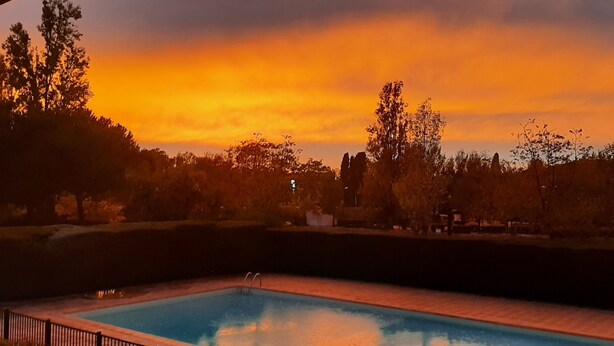 Une piscine avec vue sur le coucher de soleil, entourée d’arbres et d’une clôture.