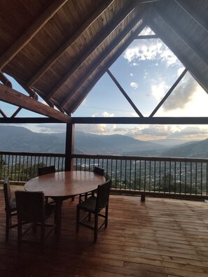 Une terrasse en bois avec une table ronde et des chaises, offrant une vue sur un paysage montagneux.