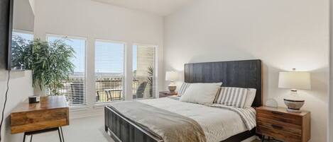 A bedroom with a bed, bedside tables, a desk, and a large window with blinds.