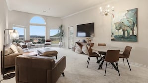 A spacious living room with a large window, a dining area with a table and chairs, and a mounted flat-screen TV. - The Troubadour at Tapatio Springs- Golf, Swimming Pool, Restaurant & Bar. (Boerne)
