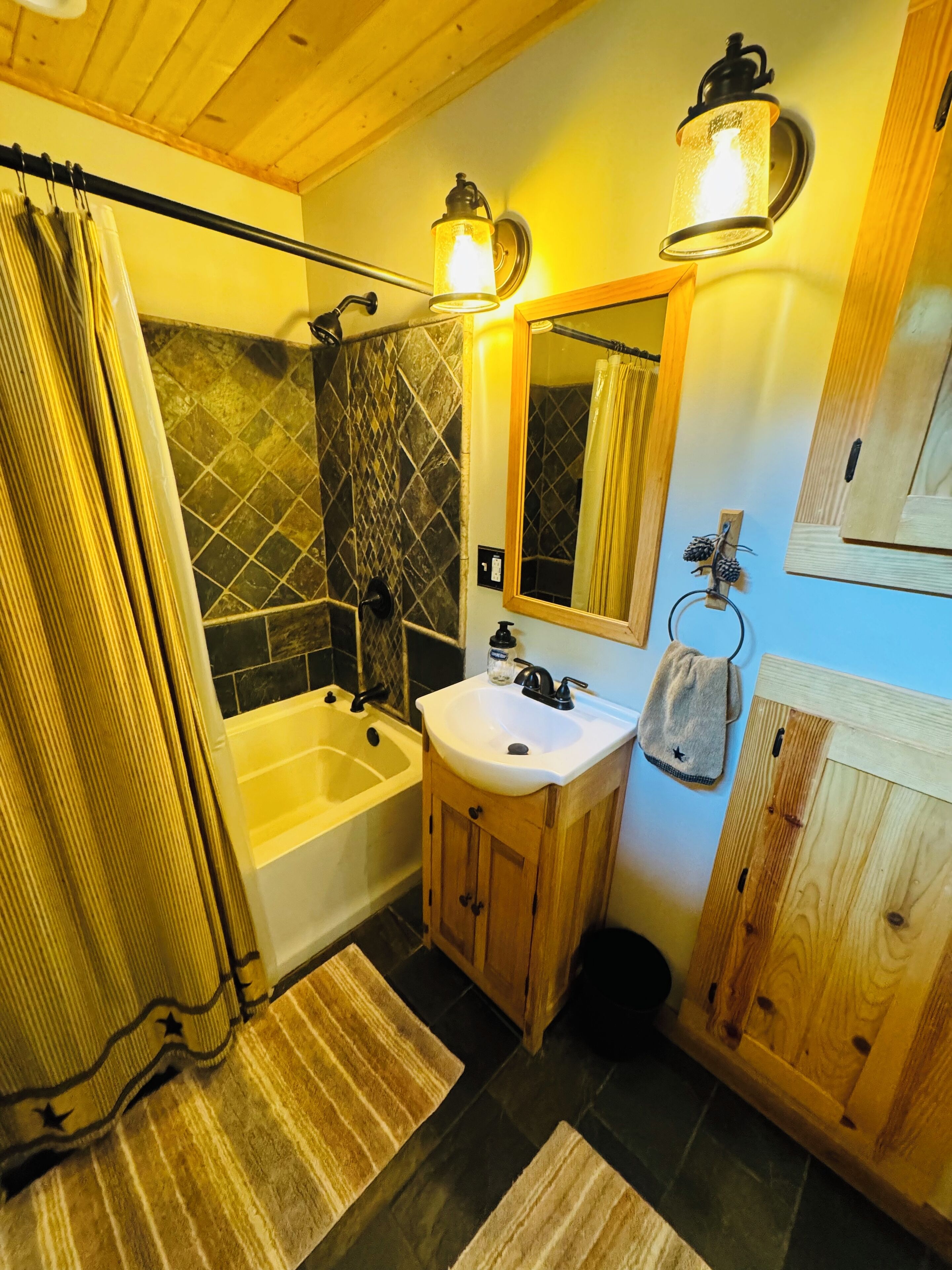 Une salle de bain avec une baignoire, un lavabo et un miroir. On y trouve un rideau de douche, un porte-serviettes et un meuble en bois.