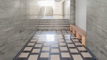 Un pasillo moderno con suelo a cuadros, paredes de mármol y una escalera que lleva a un nivel superior.