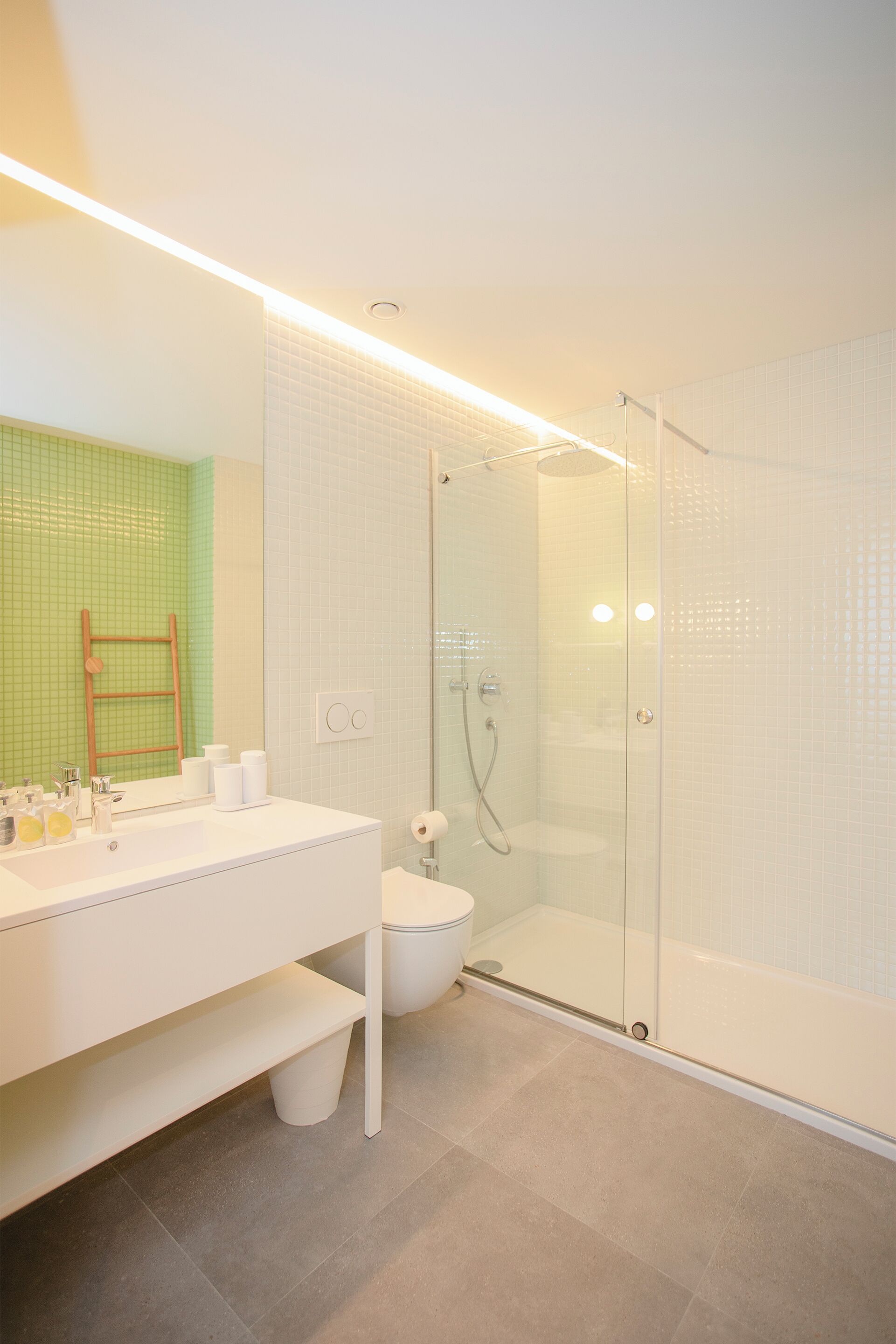 A modern bathroom with a glass-enclosed shower, a white vanity with a mirror, and a green-tiled wall.