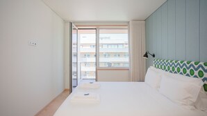 A hotel room with a large bed, a window with curtains, a view of buildings, and a wall with a patterned headboard. - Allegro Boutique Apartment A (Porto)